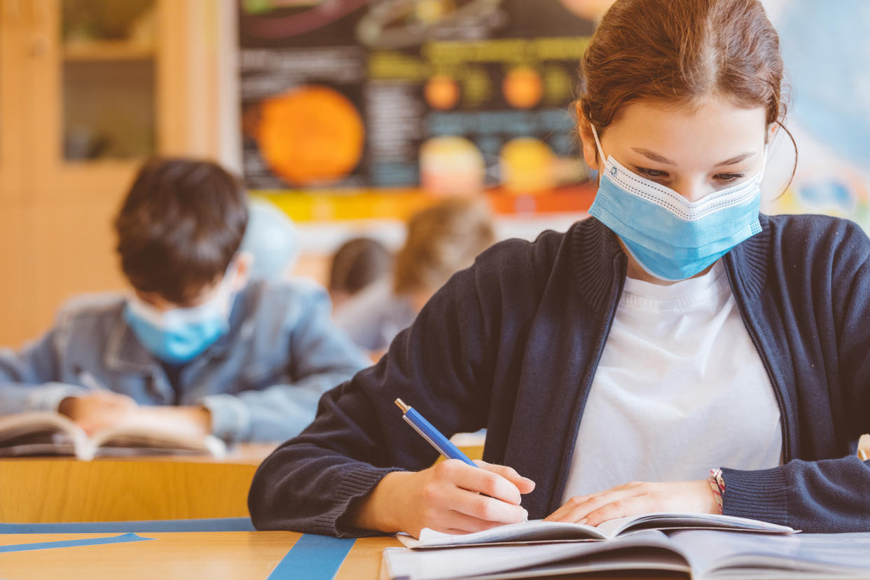 High school students at school, wearing N95 Face masks. Teenage girl wearing eyeglasses sitting at the school desk and reading book.