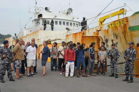 Indonesian navy soldiers hold rifles as they stand next to the detained crew of the STS-50 fishing boat at a port in Sabang, Indonesia April 7, 2018. Antara Foto/Ampelsa/via REUTERS