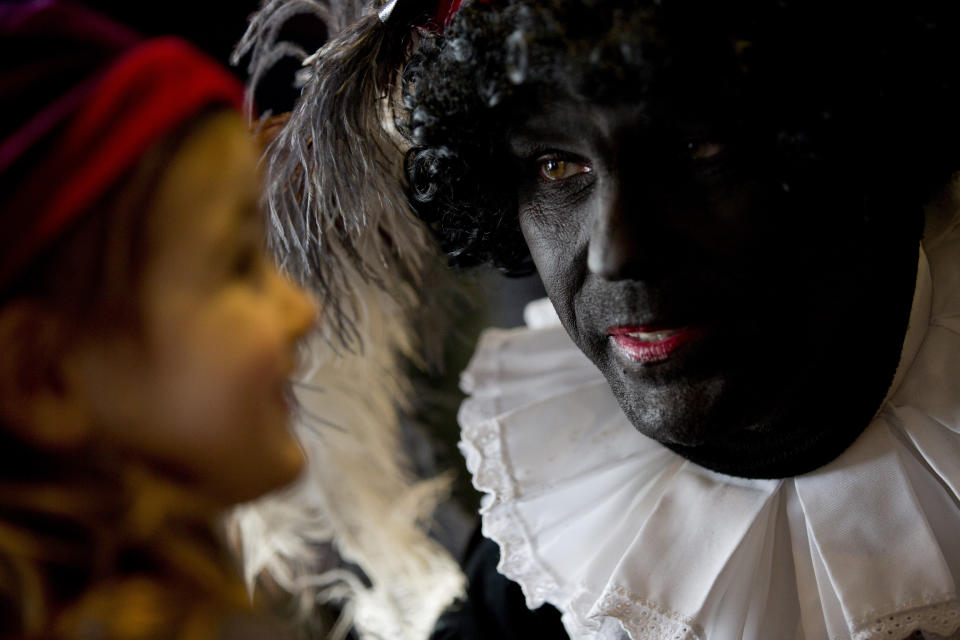 In this Friday Dec. 5, 2014 file photo three-and-a-half-year-old Ita Krans, left, talks to Black Pete, the black-faced sidekick of Sinterklaas, the Dutch version of Santa Claus, during a short ceremony at the mayor's office in Amsterdam, Netherlands. As many Dutch children eagerly anticipate the arrival of their country's version of Santa Claus this weekend, opponents and supporters of his controversial helper Black Pete are gearing up for protests. Black Pete is often played by white people with their faces daubed in dark makeup. Supporters see him as a traditional children's character, while opponents decry him as a racist stereotype. (AP Photo/Peter Dejong)