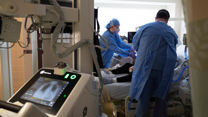دو تکنسین اشعه ایکس از قفسه سینه یک بیمار کووید در تخت بیمارستان عکس می گیرند.