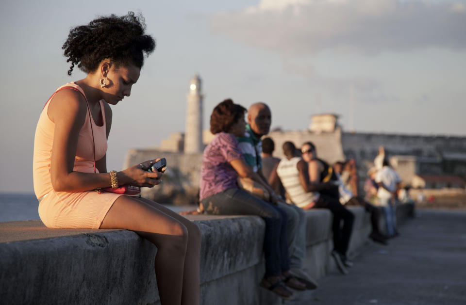 In this March 11, 2014 photo, a woman uses her cellphone as she sits on the Malecon in Havana, Cuba. The U.S. Agency for International Development masterminded the creation of a "Cuban Twitter," a communications network designed to undermine the communist government in Cuba, built with secret shell companies and financed through foreign banks, The Associated Press has learned. The project, which lasted more than two years and drew tens of thousands of subscribers, sought to evade Cuba’s stranglehold on the Internet with a primitive social media platform. (AP Photo/Franklin Reyes)