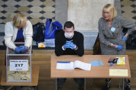 Volunteers wearing masks and gloves wait for voters in a polling station during local elections in Lyon, central France, Sunday, March 15, 2020. France is holding nationwide elections Sunday to choose all of its mayors and other local leaders despite a crackdown on public gatherings because of the new virus. For most people, the new coronavirus causes only mild or moderate symptoms. For some it can cause more severe illness. (AP Photo/Laurent Cipriani)