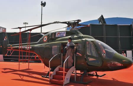 A woman poses for a photograph next to an Indian Air Force (IAF) light utility helicopter on display at the Aero India air show at Yelahanka air base in the southern Indian city of Bengaluru February 18, 2015. REUTERS/Abhishek N. Chinnappa