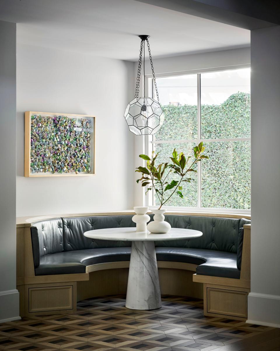 The breakfast nook by the open kitchen has a circular white-oak banquette with leather cushions and a round marble table from the 1920s, purchased at M.Naeve antiques in Houston. The multifaceted bronze-and-glass fixture is from Rose Uniacke.