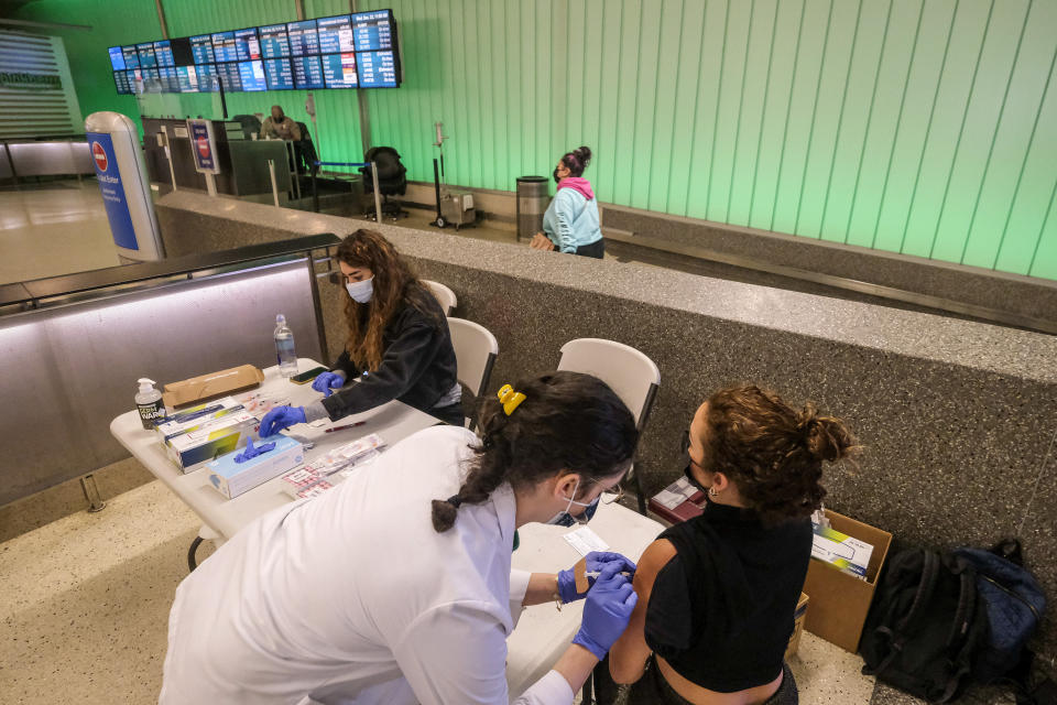 Traveler Ana Paula Gonzalez, right, of Mexico, is vaccinated at the Los Angeles International Airport in Los Angeles, Wednesday Dec. 22, 2021. People traveling during the holiday season can get free COVID-19 vaccinations and booster shots at LAX on two consecutive Wednesdays -- today and Dec. 29. The pop-up clinic, located at the Lower/Arrivals Level of the Tom Bradley International Terminal, will be open from 11 a.m. to 5 p.m. on the two days. (AP Photo/Ringo H.W. Chiu)