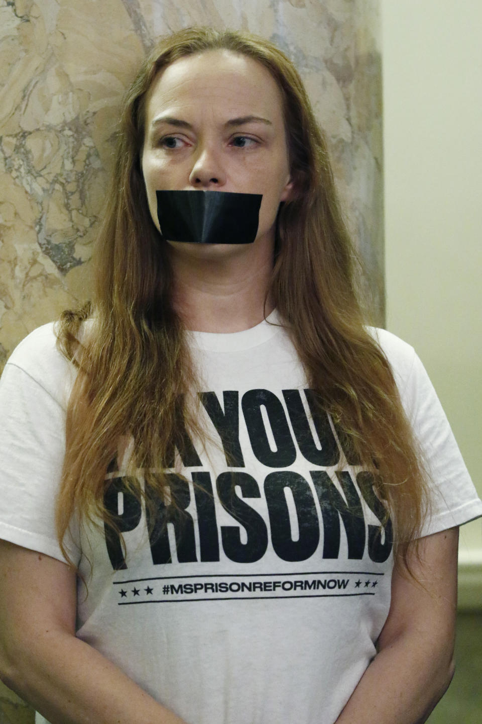 Danielle Quiterio, one of a couple of dozen prison reform advocates, who wore a strip of tape across their mouth as a form of silent protest, stands during a joint hearing of the House Corrections and Judiciary B Committees, Thursday, Feb. 13, 2020 at the Capitol in Jackson, Miss. (AP Photo/Rogelio V. Solis)