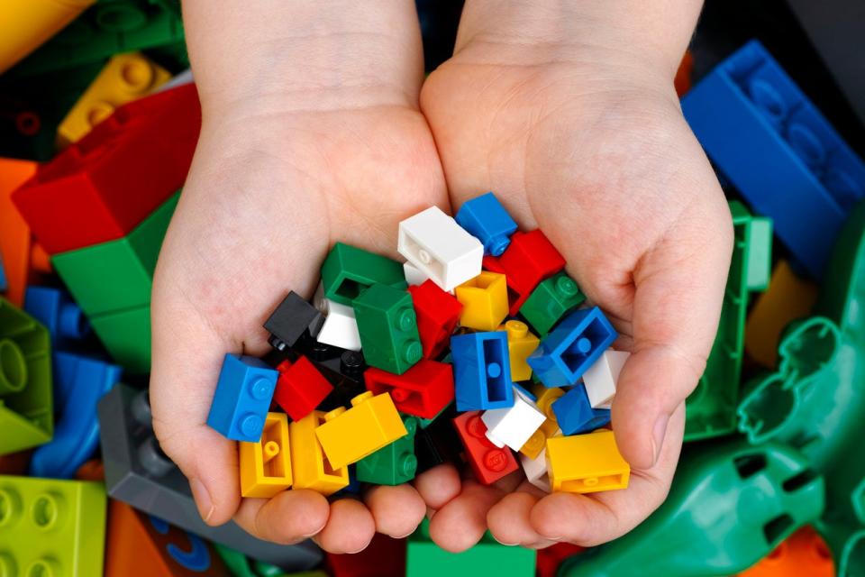 overhead close shot of a child's hands holding a bunch of small lego pieces with a pile of legos underneath. 
