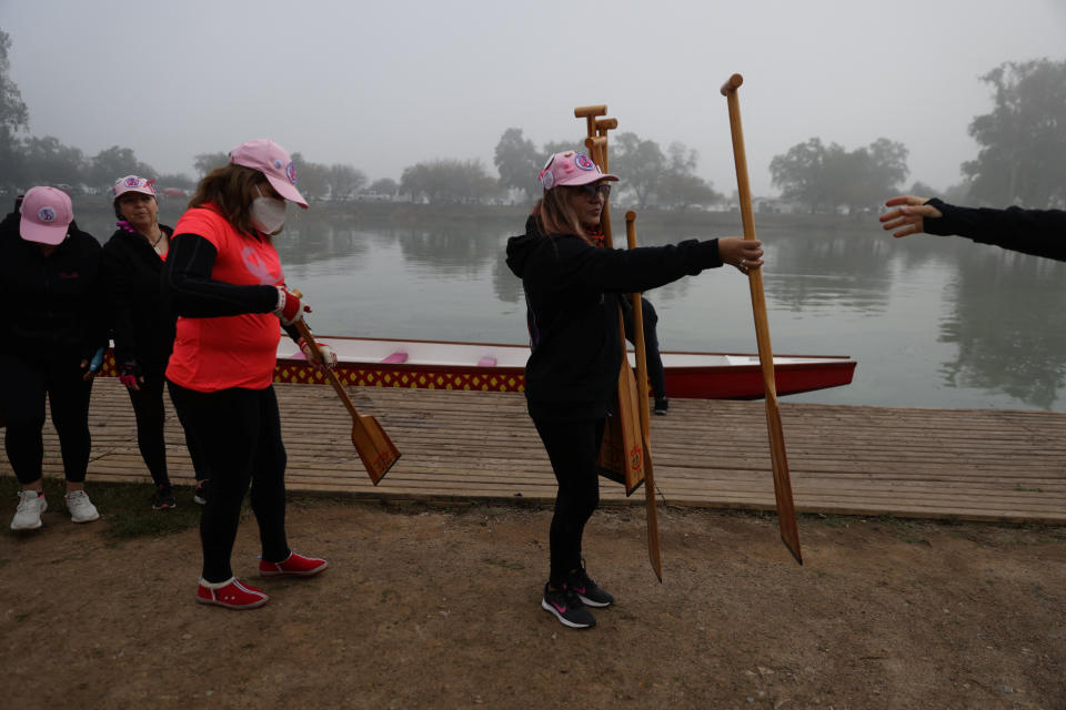 Un miembro de un equipo de remo de botes de dragón, para mujeres con cáncer de mama y sobrevivientes, entrega palas de remo a sus compañeros de equipo antes de una sesión de entrenamiento en una laguna en las afueras de Santiago, Chile, 24 de julio de 2022. (REUTERS/Ivan Alvarado)