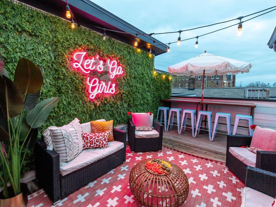 A patio with a faux greenery wall and a neon sign that says "let's go girls."