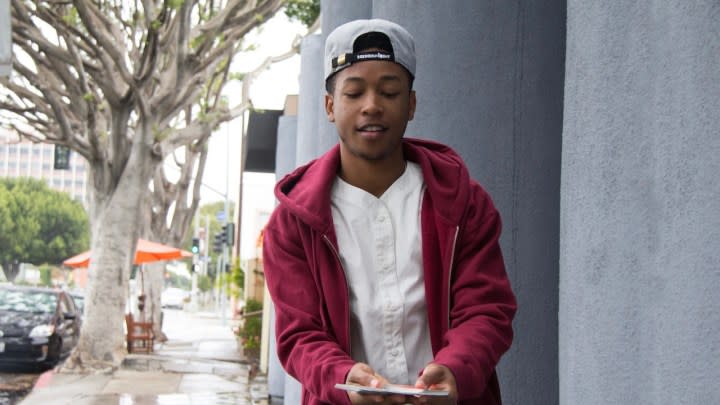 Jacob Latimore walks down the street holding cards.