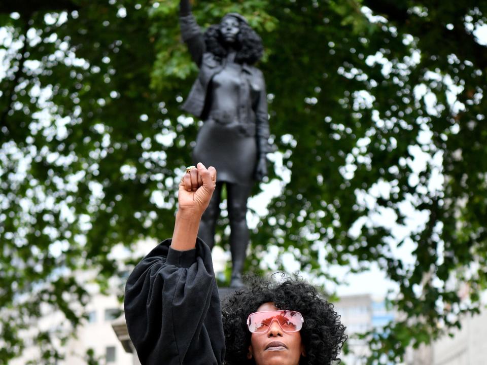 BRISTOL, ENGLAND - JULY 15: Black Lives Matter protestor Jen Reid poses for a photograph in front of a sculpture of herself, by local artist Marc Quinn, on the plinth where the Edward Colston statue used to stand on July 15, 2020 in Bristol, England. A statue of slave trader Edward Colston was pulled down and thrown into Bristol Harbour during Black Lives Matter protests sparked by the death of an African American man, George Floyd, while in the custody of Minneapolis police in the United States of America. The Mayor of Bristol has since announced the setting up of a commission of historians and academics to reassess Bristol's landmarks and buildings that feature the name of Colston and others who made fortunes in trades linked to slavery. (Photo by Matthew Horwood/Getty Images)