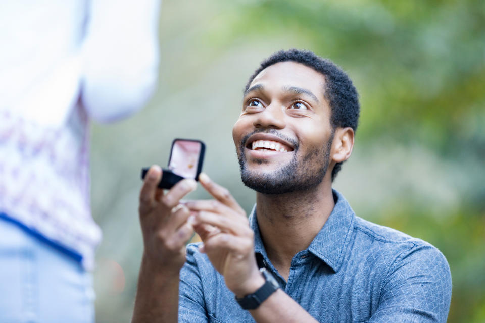 Man proposing to partner with ring, both smiling, in a natural setting