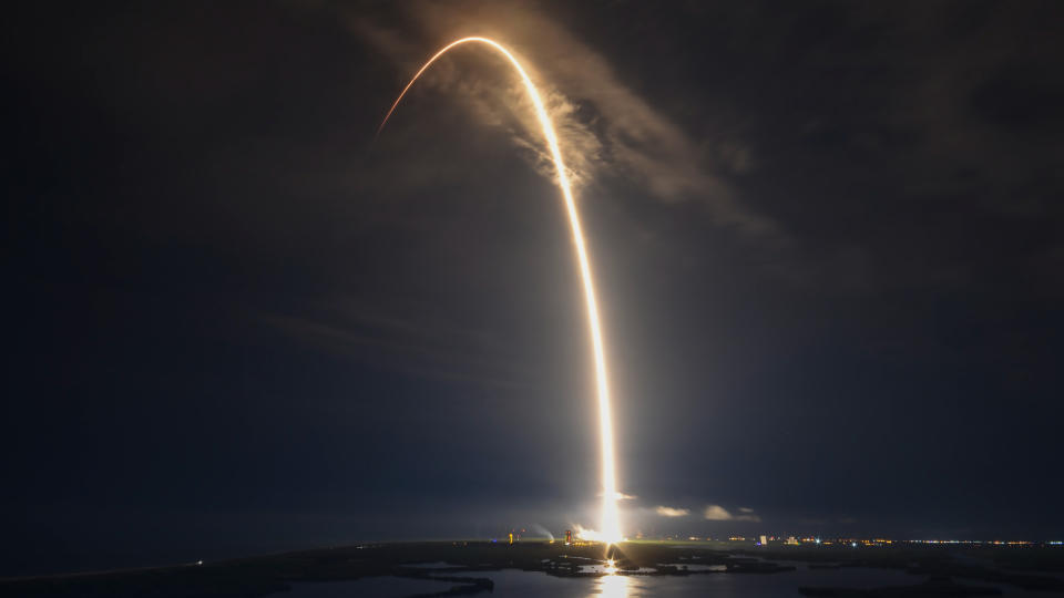 a spacex falcon 9 rocket makes a yellow-orange arc in a dark sky during launch
