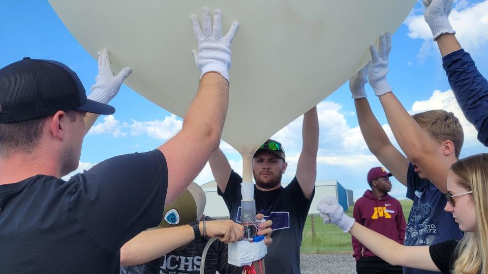 People gather around a large white balloon, they are holding it up.