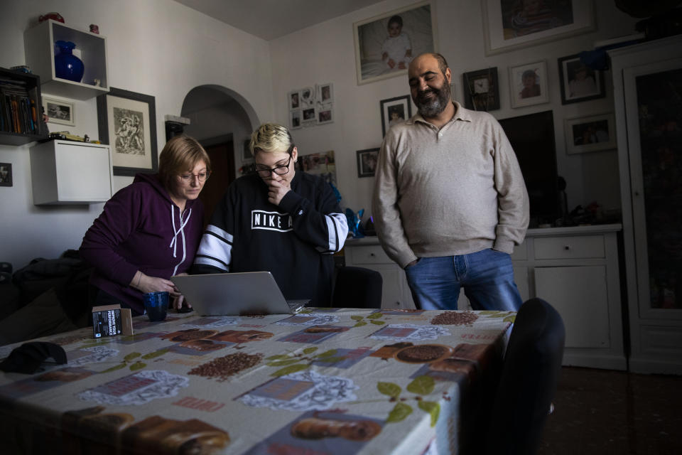 Matteo is flanked by his parents, Monica Fragala, left, and Franco Coccimiglio, in their kitchen in Rome, Saturday, March 20, 2021. Matteo Coccimiglio is an 18-year-old student who identifies as a man and is in the process of changing his legal gender from female to male. The Ripetta school of art in Rome - where he studies - recently joined a handful of high schools in Italy that give transgender students the right to be known by a name other than the one they were given at birth. The initiative is meant to create an environment where transgender students feel secure and reflects a growing awareness in Italy of gender dysphoria among teenagers and children. (AP Photo/Alessandra Tarantino)