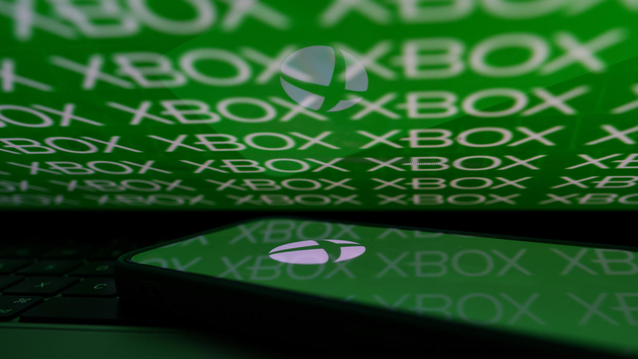  A phone with an Xbox logo reflected in a looming laptop monitor. 