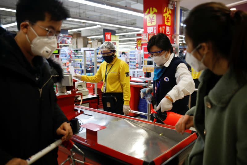 A staff member wearing a face mask sanitizes a cashier counter at a supermarket, as the country is hit by an outbreak of the new coronavirus, in Beijing