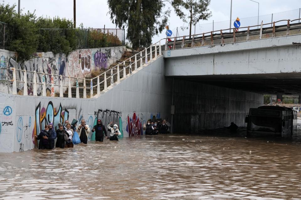 Passengers wade through high water after evacuating a bus stuck in a flooded underpass in southern Athens, Thursday, Oct. 14, 2021. Storms have been battering the Greek capital and other parts of southern Greece, causing traffic disruption and some road closures. (AP Photo/Thanassis Stavrakis)