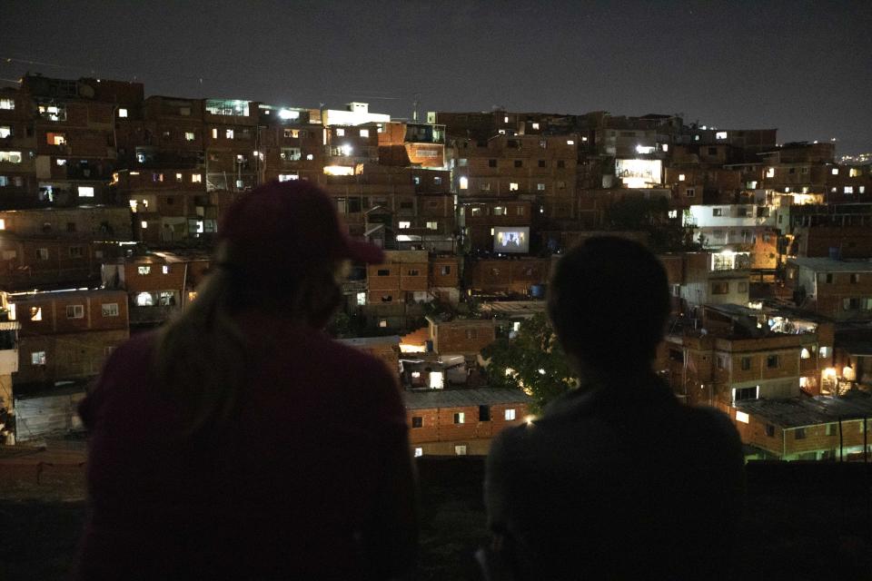 People watch the movie Aladdin projected on a screen set up on the roof of a home, center right, in the Petare neighborhood of Caracas, Venezuela, late Monday, June 1, 2020. A neighborhood group called The Download Zone set up the movie as a free entertainment option for families cooped up since mid-March under the COVID-19 quarantine. (AP Photo/Ariana Cubillos)