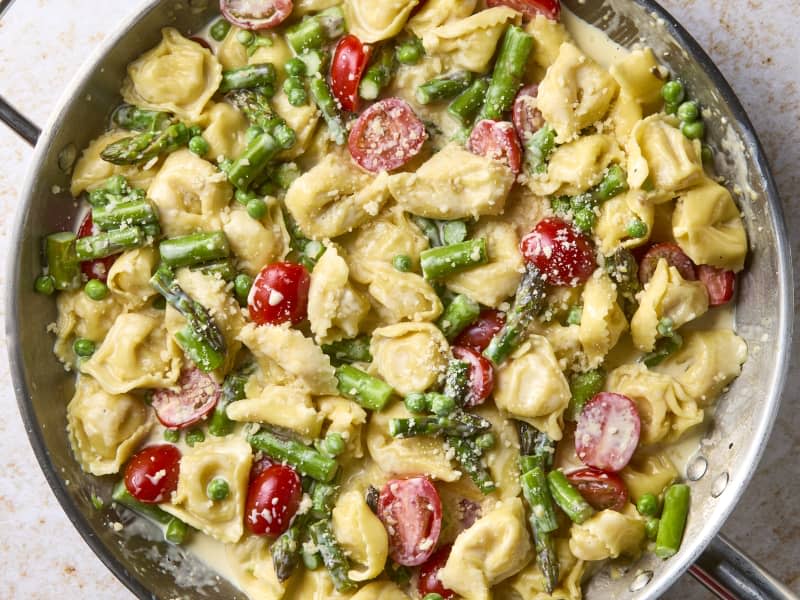 overhead shot of creamy tortellini primavera, topped with cheese, in a pan