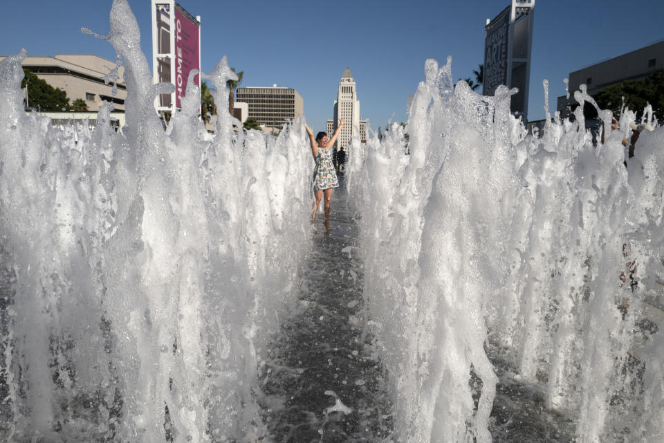 FILE - A visitor takes photos at the newly renovated water fountain at the Los Angeles Music Center's plaza on Aug. 29, 2019, with city hall seen in the background. The sight of fountains, swimming pools, gardens and golf courses in Western cities like Phoenix, Los Angeles, Las Vegas, San Diego and Albuquerque can seem jarring with drought and climate change tightening their grip on the region. But Western water experts say they aren’t necessarily cause for concern. Many Western cities over the past three decades have diversified their water sources, boosted local supplies, and use water more efficiently now than in the past. (AP Photo/Richard Vogel, File)