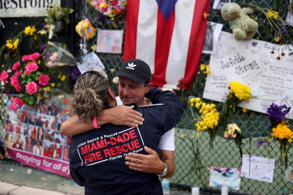 SURFSIDE, FLORIDA - JULY 07: Search and Rescue personnel Maggie Castro (L) hugs Pablo Langesfeld as they visit the memorial to the victims in the collapsed 12-story Champlain Towers South condo building as the search and rescue efforts are reported be transitioning to a recovery operation on July 07, 2021 in Surfside, Florida. Mr. Langesfeld daughter Nicole Langesfeld is one of the missing in the collapse of the building. Officials say the death toll climbed to 46, with 94 still unaccounted for. (Photo by Joe Raedle/Getty Images)