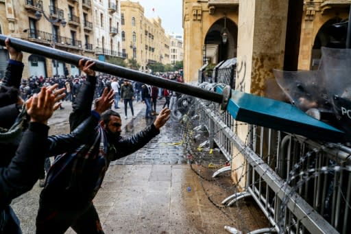 Anti-government protesters use a road sign to ram security forces taking cover during clashes near the parliament building in the Lebanese capital Beirut