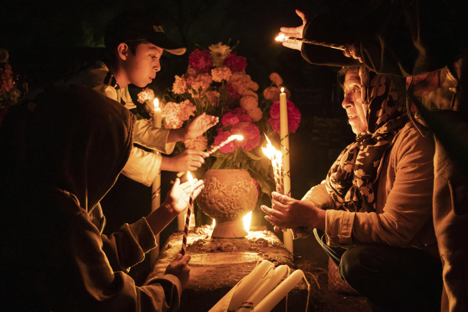 La gente sostiene velas sobre una tumba decorada con flores en un cementerio en Atzompa, México, el martes 31 de octubre de 2023 por la noche. (AP Foto/María Alferez)