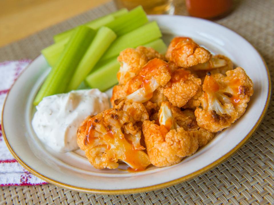 buffalo cauliflower bites on a plate with ranch and celery, with a red and white napkin on the side