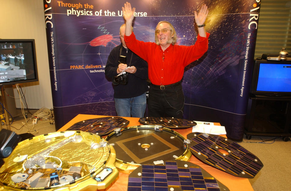 FILE - A Thursday, Dec. 25, 2003 photo from files of Professor Colin Pillinger, leading scientist for the Beagle 2 Mars landing module, gestures in a control centre in central London in front of a model of the 'pod' which landed on Mars as he waits for radio signals from the device. Pillinger, an ebullient British space scientist who captured the popular imagination with his failed attempt to land a probe on Mars, has died. He was 70. Pillinger's family said Thursday that he died at Addenbrooke's Hospital in Cambridge after suffering a brain hemorrhage while sitting in his garden in the university town. (AP Photo/Adam Butler)