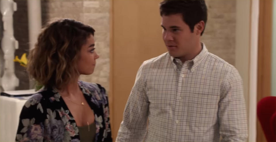 Two characters from a TV show standing side by side, the woman in a floral dress and the man in a checkered shirt