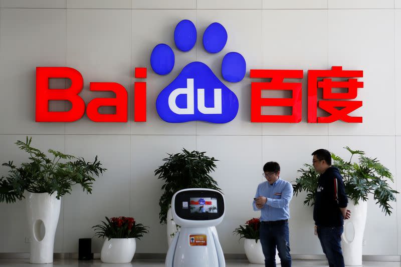 Men interact with a Baidu AI robot near the company logo at its headquarters in Beijing