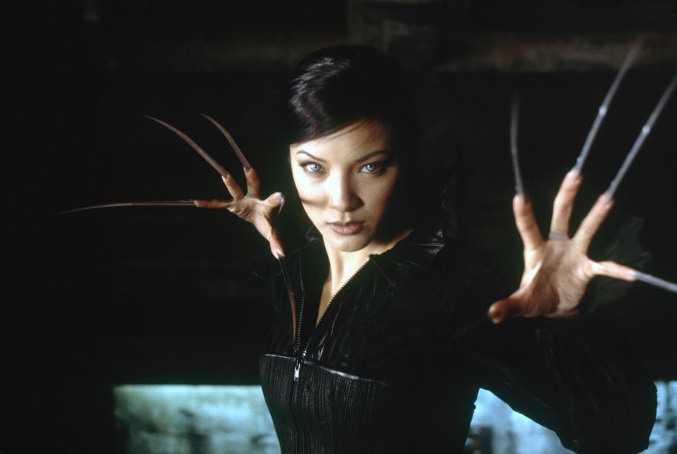 Character with metal claws posing, wearing a black leather outfit in a dimly lit setting