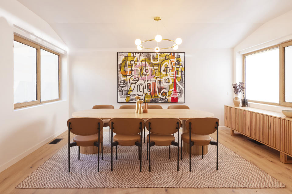 A wide shot of the dining room,  a dining table in the centre on a rug and a colourful painting on the far wall. 