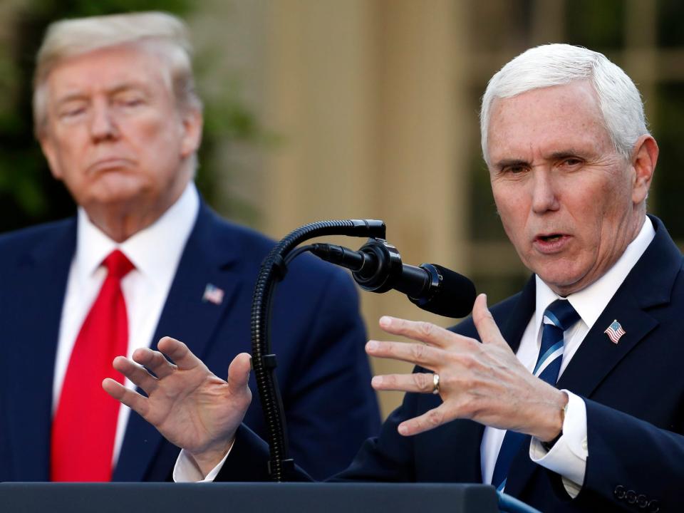 Mike Pence speaking into a microphone while standing behind a podium with his hands out in front of his chest while Donald Trump looks on from behind him.