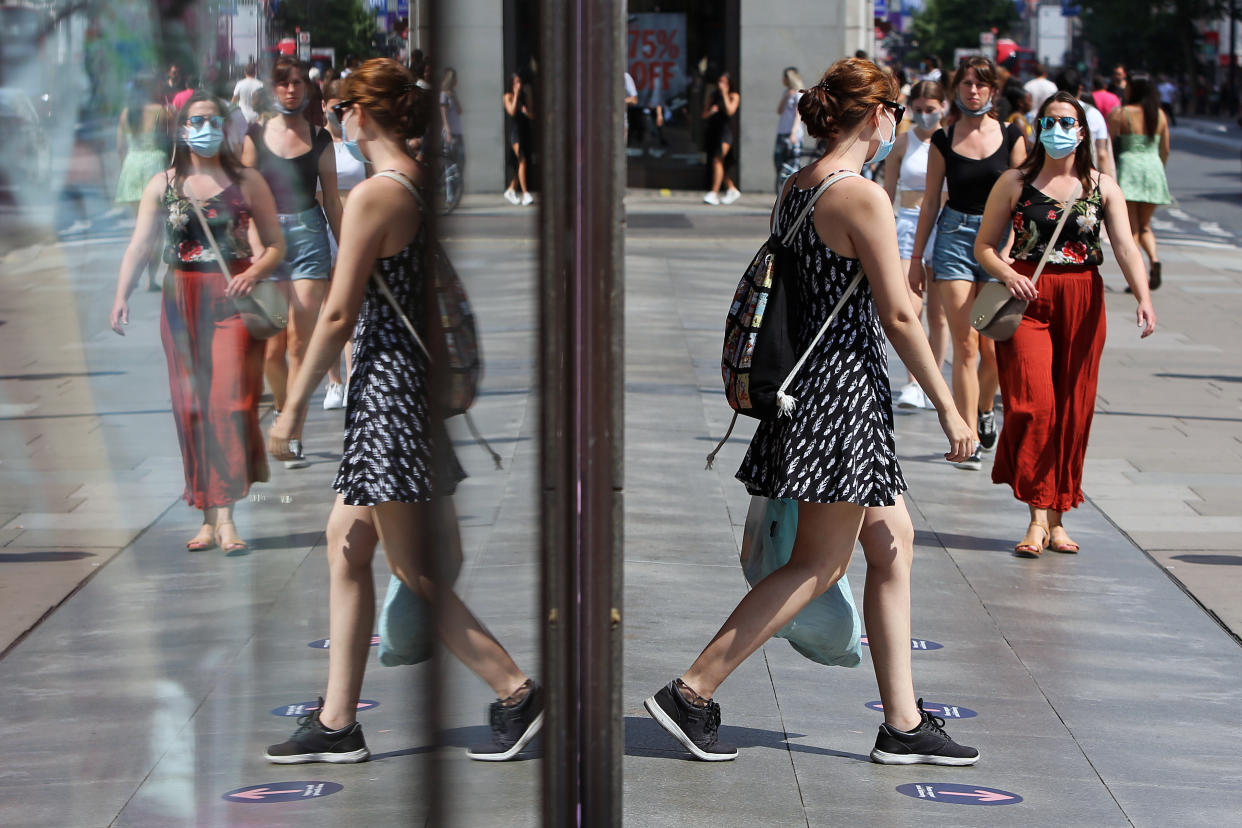 A general view of a busy Oxford Street, London, in the reflection of a shop window, as a girl walks out of a shop wearing a protective face mask due to coronavirus.