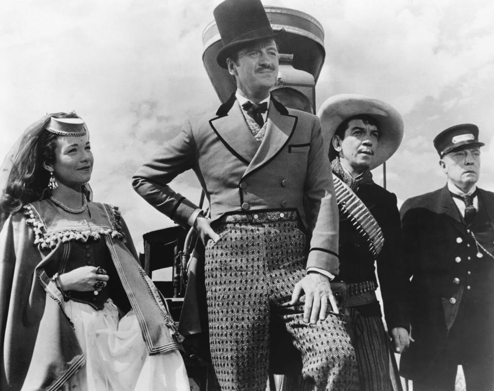 A woman and three men stand in front of a steam locomotive in "Around the World in 80 Days."