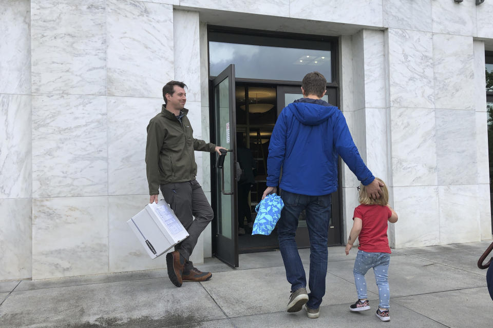 Joe Emmons, a signature gatherer for a proposed ballot measure requiring the safe storage of weapons, holds the door for a supporter as they deliver 2,000 signatures backing the proposed ballot measure on Wednesday, Sept. 18, 2019, to the state elections office in Salem, Ore. Backers of the proposal say it would reduce the number of school shootings and suicides. (AP Photo/Andrew Selsky)
