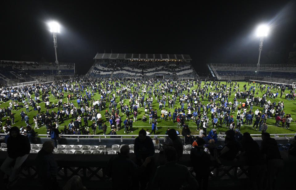 Fans of Gimnasia de La Plata take to the pitch after tear gas flooded the stadium during a local tournament soccer match between Gimnasia de La Plata and Boca Juniors in La Plata, Argentina, Thursday, Oct. 6, 2022. The match was suspended after tear gas thrown by the police outside the stadium wafted inside affecting the players as well as fans who fled to the field to avoid its effects. (AP Photo/Gustavo Garello)