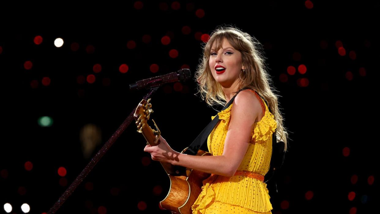 taylor swift holding a guitar and smiling as she stands in front of a microphone at a concert