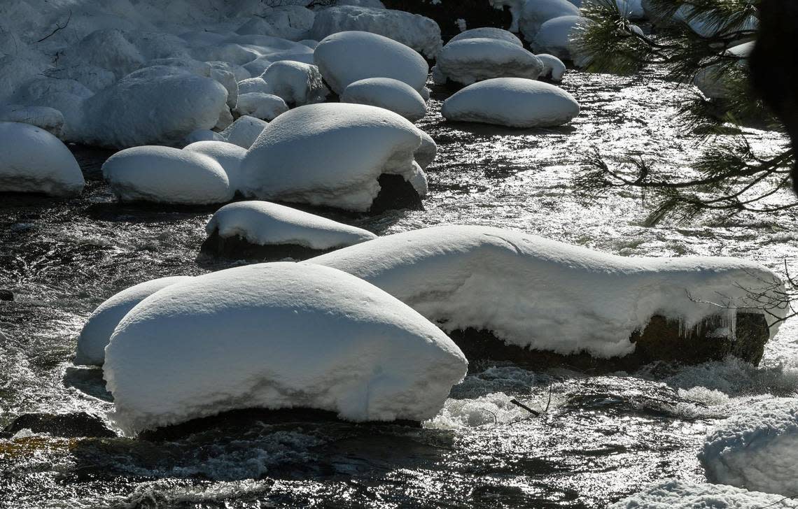 Rocks are covered in thick snow as the water of the Merced River flows by in Yosemite National Park on Friday, March 3, 2023.