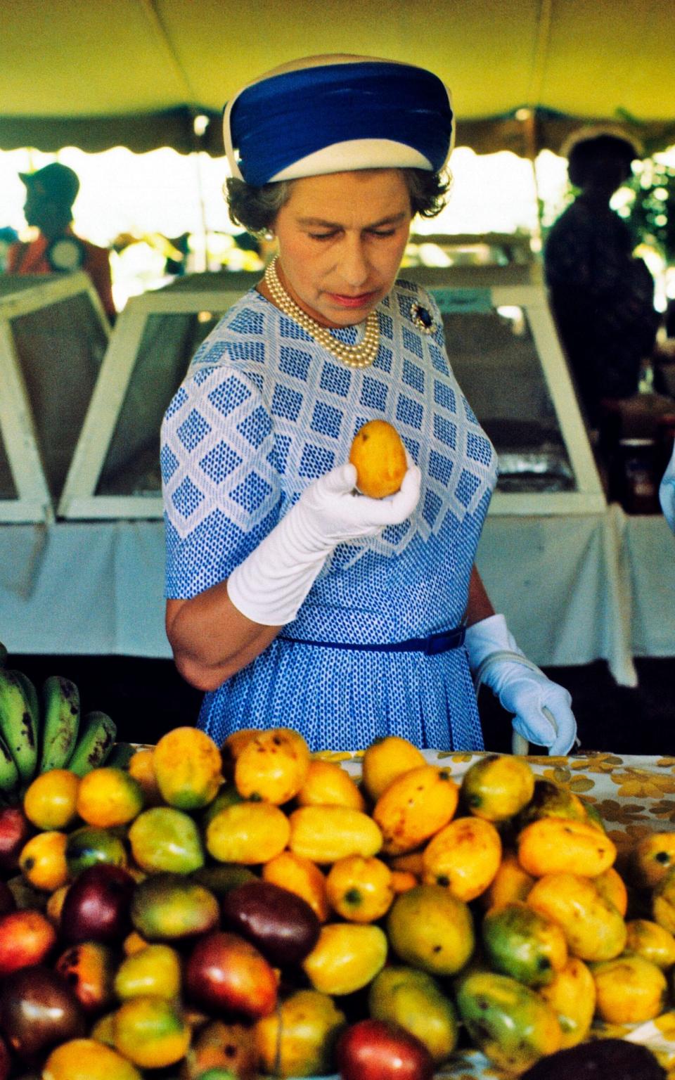 Queen Elizabeth ll picks up a mango as she tours a market in the British Virgin Islands in October of 1977. - Anwar Hussein/Getty Images