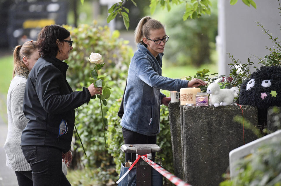 People bring flowers and candles to an apartment building, where five dead children were found in Solingen, Germany, Friday, Sept. 4, 2020. Police say five young children have been found dead on Thursday at the apartment in Solingen, their mother is suspected of killing them. Police said the children's 27-year-old mother later jumped in front of a train in Duesseldorf and was taken to a hospital with injuries. Only one child of the mother survived, who was send to his grandmother before. (AP Photo/Martin Meissner)