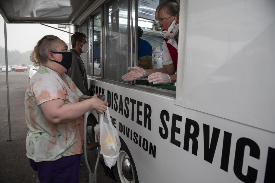 Mary Thomson, left, from Phoenix receives a hot meal from the Salvation Army Disaster relief truck at the evacuation center set up at the Jackson County Fairgrounds on Saturday, Sept. 12, 2020 in Central Point, Ore. They lost their home to the destructive wildfires devastating the region. (AP Photo/Paula Bronstein)