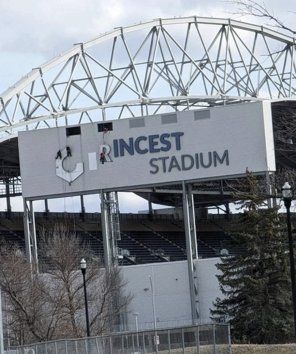 Workers repair a stadium sign where some letters are missing or covered