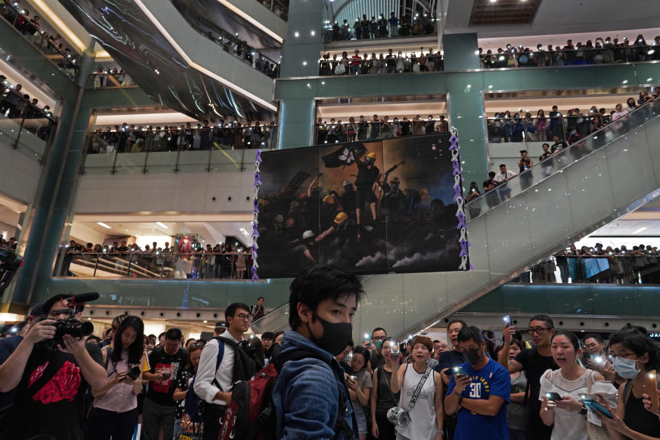 A protester raises a painting of protesters after they sing a theme song written by protesters "Glory be to thee" at a shopping mall in Hong Kong Wednesday, Sept. 11, 2019. Hundreds of Hong Kong citizens gathered at several malls late Wednesday, chanting slogans and belting out a new protest song. The song, "glory to Hong Kong", was penned online and has been embraced by protesters as their anthem song. The peaceful mall gatherings marked a respite after violent clashes over the weekend. (AP Photo/Vincent Yu)