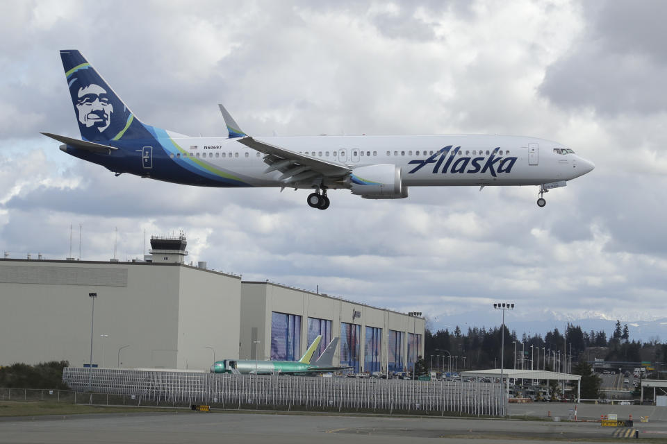 An Alaska Airlines Boeing 737-9 Max flies over Boeing's manufacturing facility in Everett, Wash., Monday, March 23, 2020, north of Seattle. All 737 Max planes remain grounded after two deadly crashes, but test and positioning flights continue to be made. Boeing announced Monday that it will be suspending operations and production at its Seattle area facilities due to the spread of the new coronavirus. (AP Photo/Ted S. Warren)