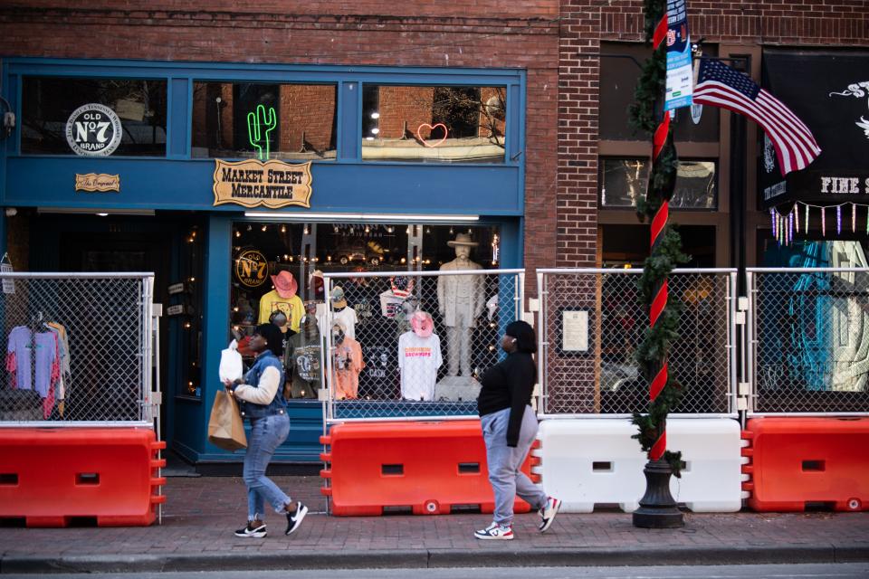 Pedestrians walk around the construction barriers along Second Avenue passing the local business in Nashville, Tenn., Tuesday, Dec. 19, 2023.