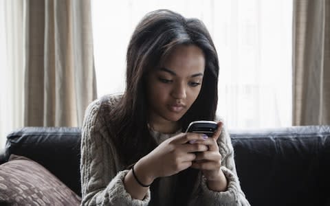 Teenage girl sitting on sofa texting on smartphone - Credit: Tom Odulate/Getty Creative