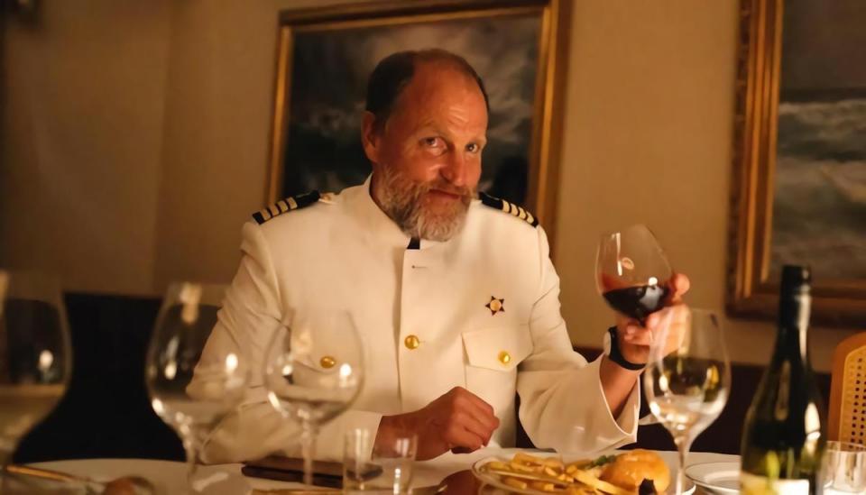 Woody Harrelson in a captain's uniform holding a glass of wine